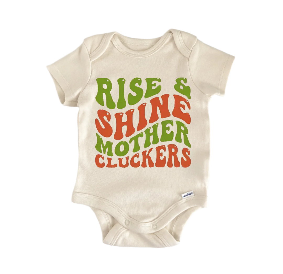 A beige baby onesie with the text "RISE & SHINE MOTHER CLUCKERS" printed on it in a vibrant, retro-style font.