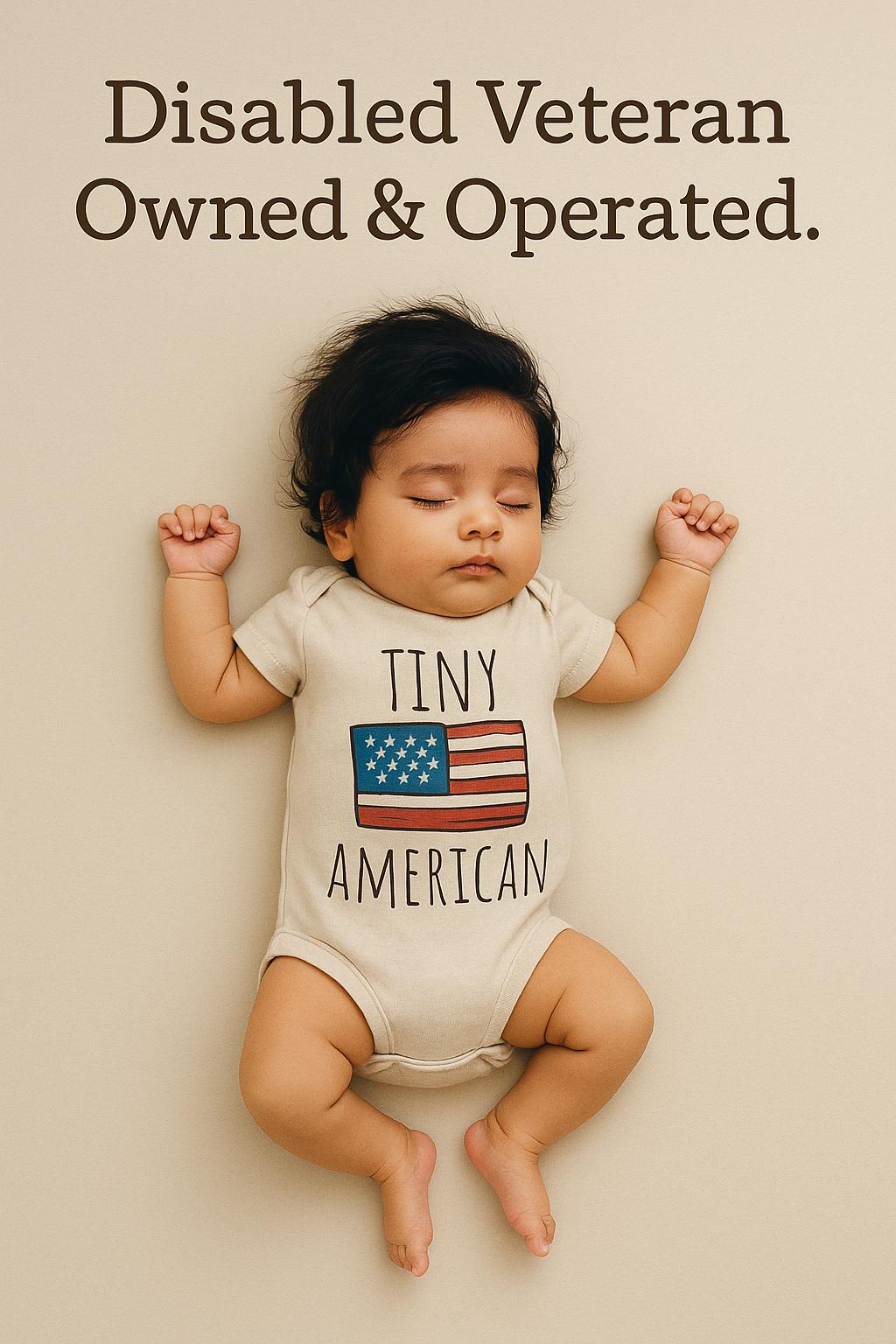 A sleeping baby wearing a white onesie with the text "Tiny American" printed on it.