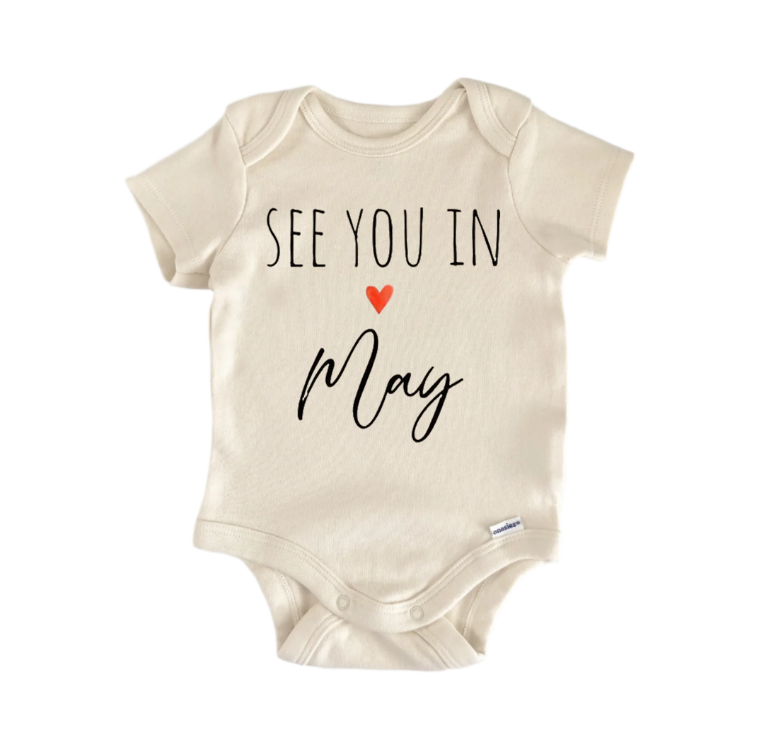 A beige baby onesie with the text "See you in May" printed on it.