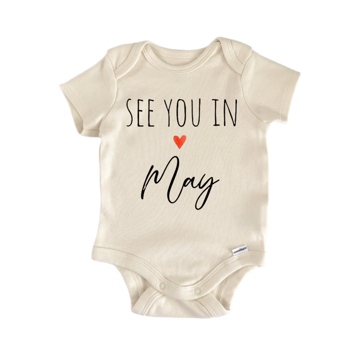 A beige baby onesie with the text "See you in May" printed on it.