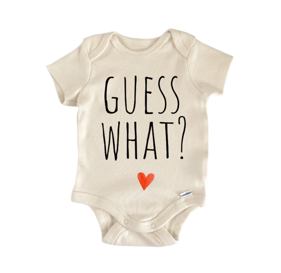 A beige baby onesie with the text "GUESS WHAT?" printed on it.