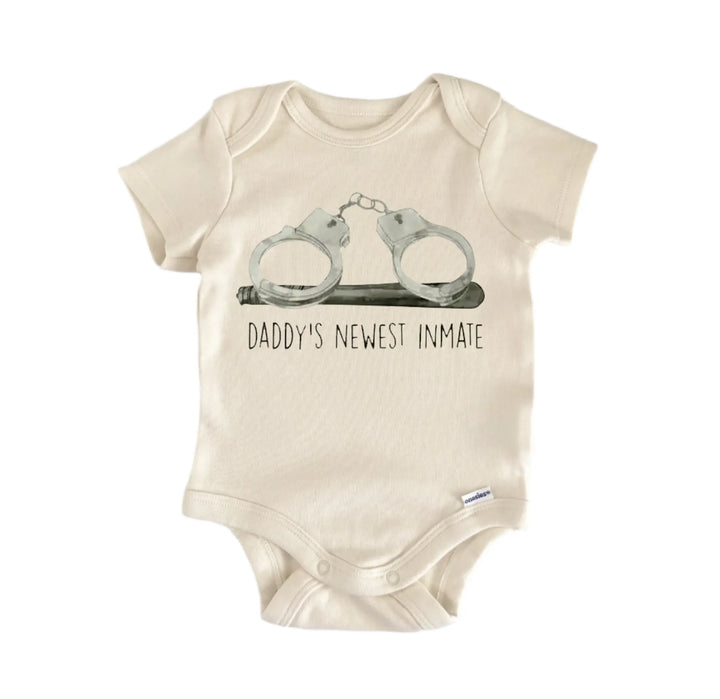 A beige baby onesie with a graphic of two handcuffs and the text "DADMY&