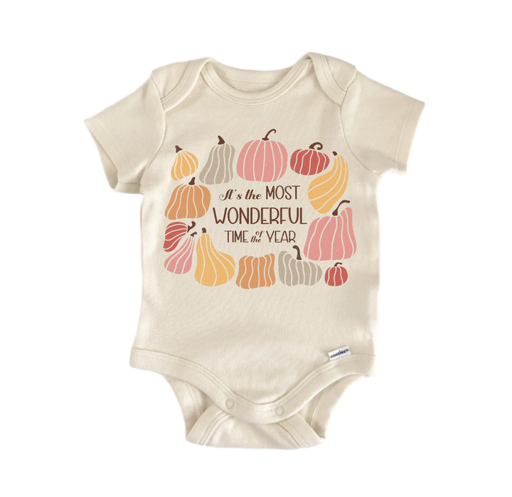 A beige baby onesie with a graphic design featuring various pumpkins and the text "It's the most wonderful time of year" printed on it.