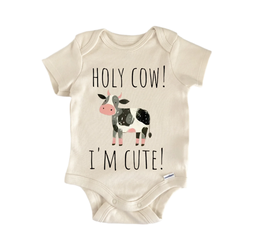 A beige baby onesie with a cartoon cow and the text "HOLY COW! I'M CUTE!" printed on it.