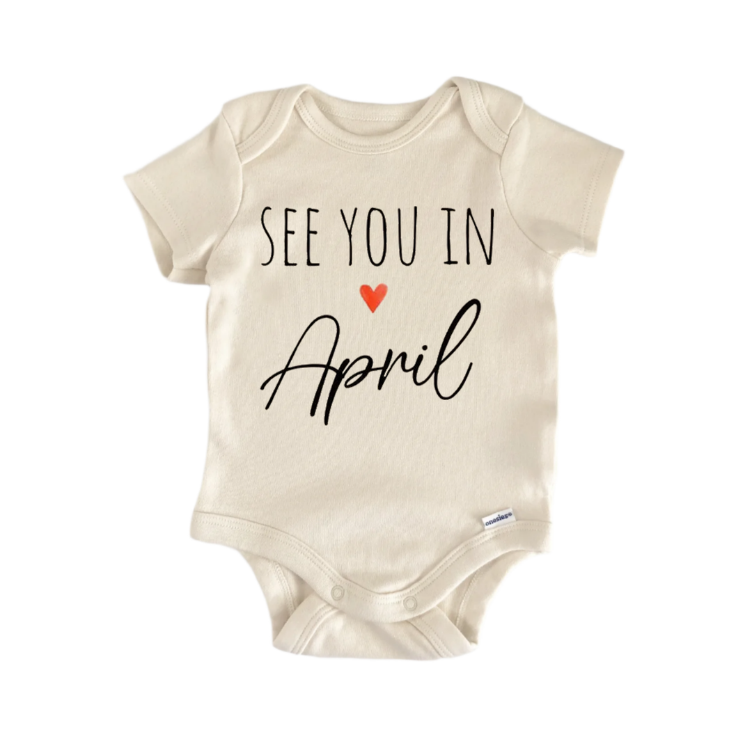 A beige baby onesie with the text "See you in April" printed on it.