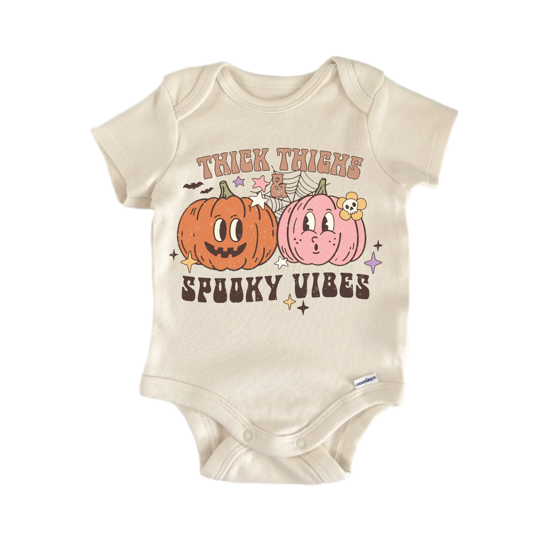 A beige baby onesie with a Halloween-themed graphic design. The design features two cartoon pumpkins, one orange and one pink, along with a spider web and stars. The text on the shirt reads "Thick Thighs SPooky Vibes".