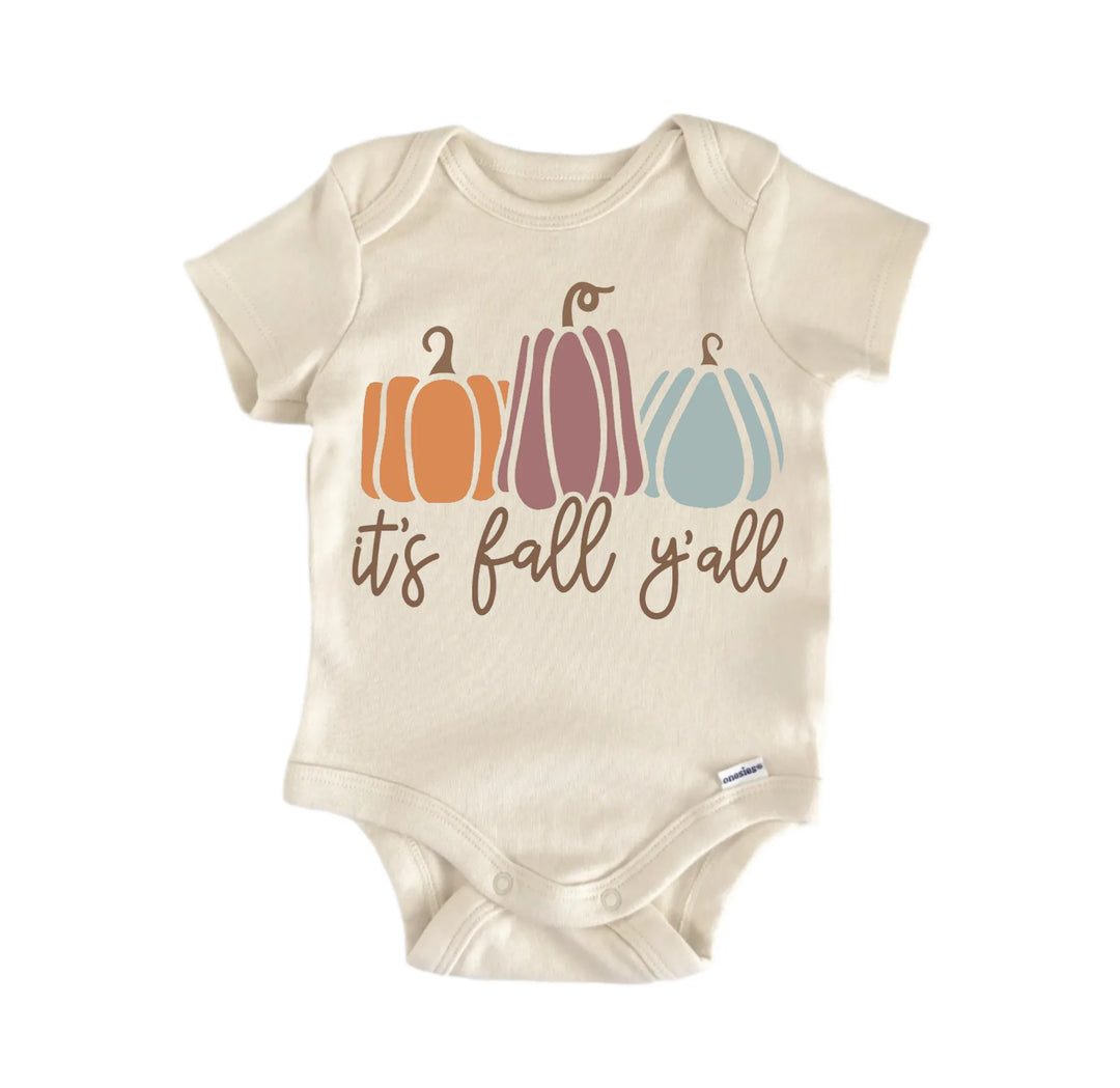 A beige baby onesie with a graphic design featuring three pumpkins in different colors and the text "it&