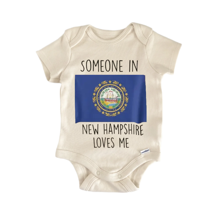 A beige baby onesie with the text "SOMEONE IN NEW HAMPSHIRE LOVES ME" printed on it, along with a small image of the state of New Hampshire's coat of arms.