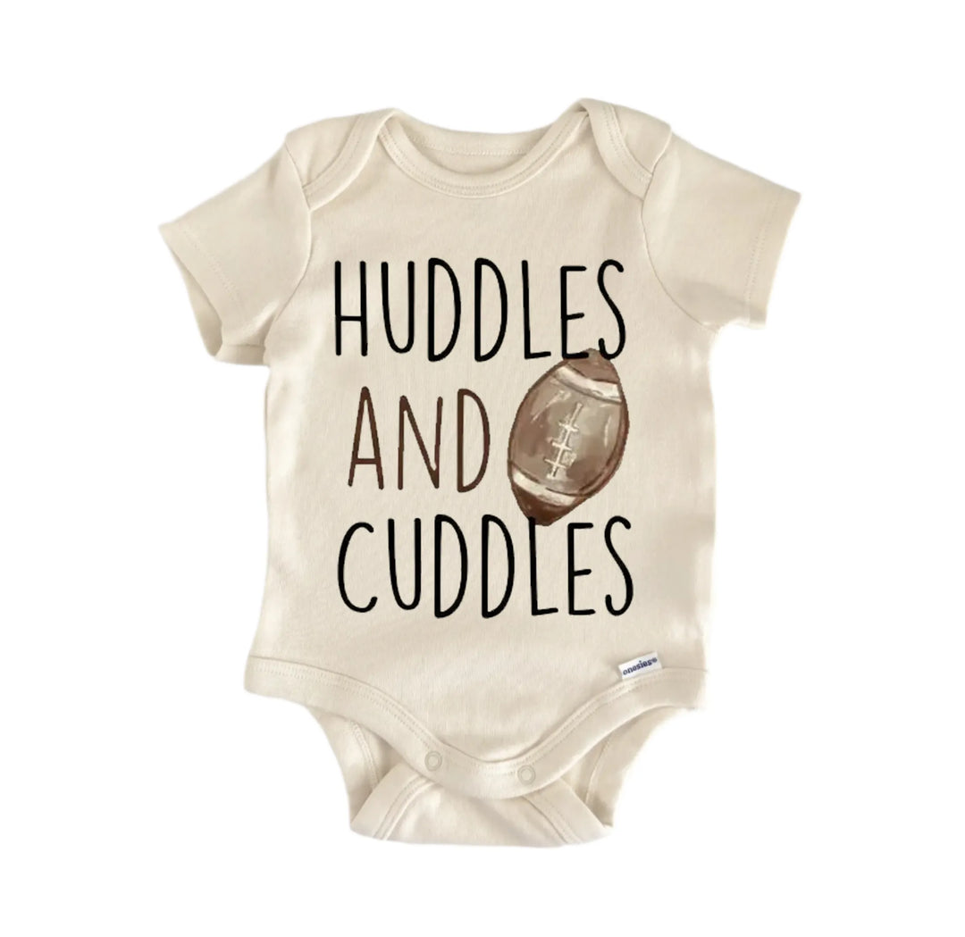 A beige baby onesie with the text "Huddles and Cuddles" printed on it, along with an image of a football.