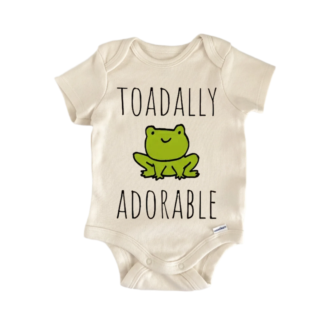 A beige baby onesie with a green frog graphic and the text "Toadally adorable" printed on it.