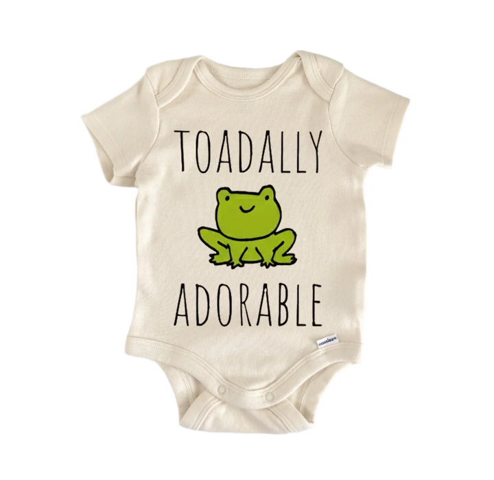 A beige baby onesie with a green frog graphic and the text "Toadally adorable" printed on it.
