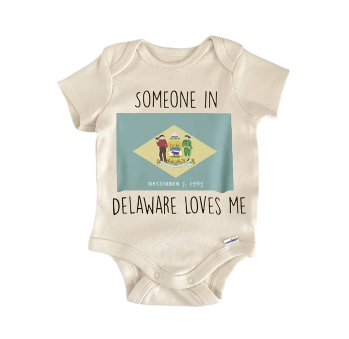 A beige baby onesie with a graphic of the Delaware state flag and the text "SOMEONE IN DELAWARE LOVES ME" printed on it.