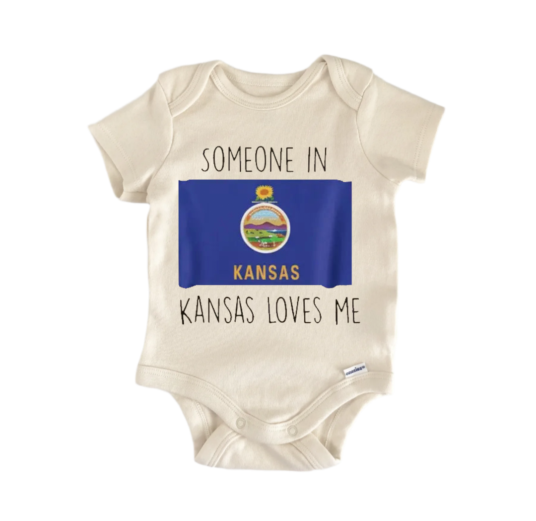 A beige baby onesie with a blue Kansas state flag and the text "SOMEONE IN KANSAS KANSAS LOVES ME" printed on it.