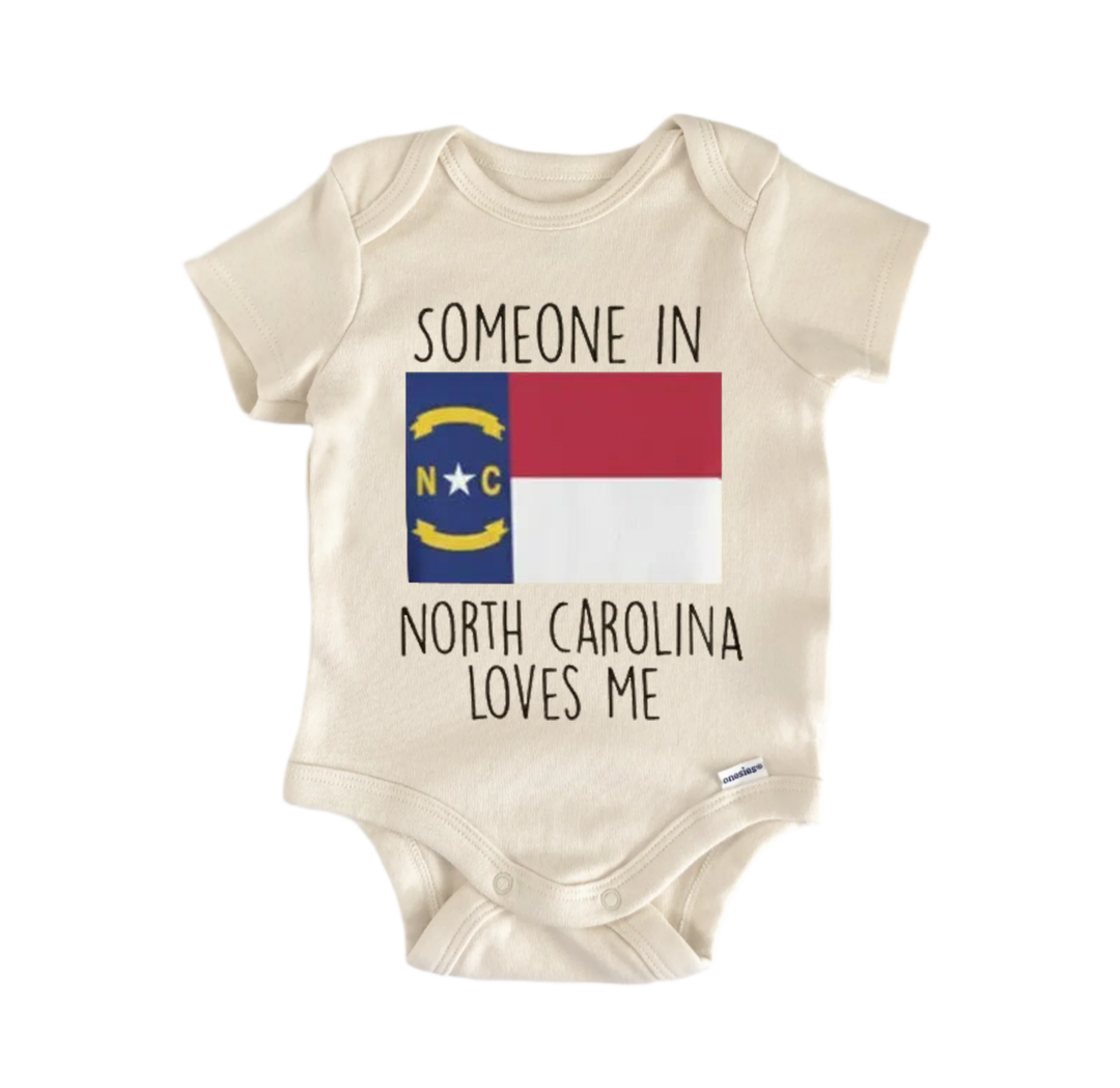 A beige baby onesie with the text "SOMEONE IN NORTH CAROLINA LOVES ME" printed on it, along with the flag of North Carolina.
