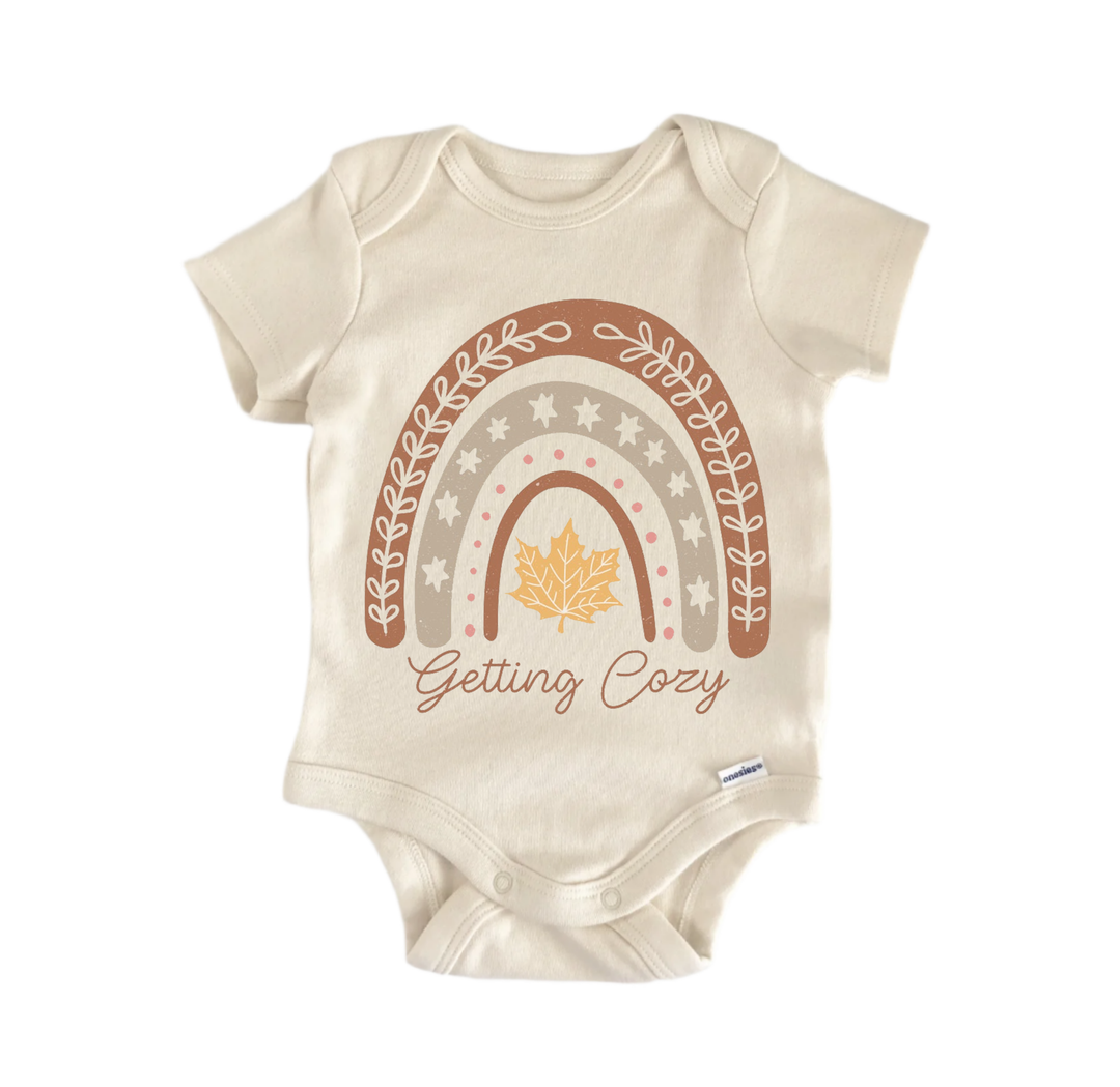A beige baby onesie with a graphic design featuring a rainbow and a leaf, along with the text "Getting Cozy".