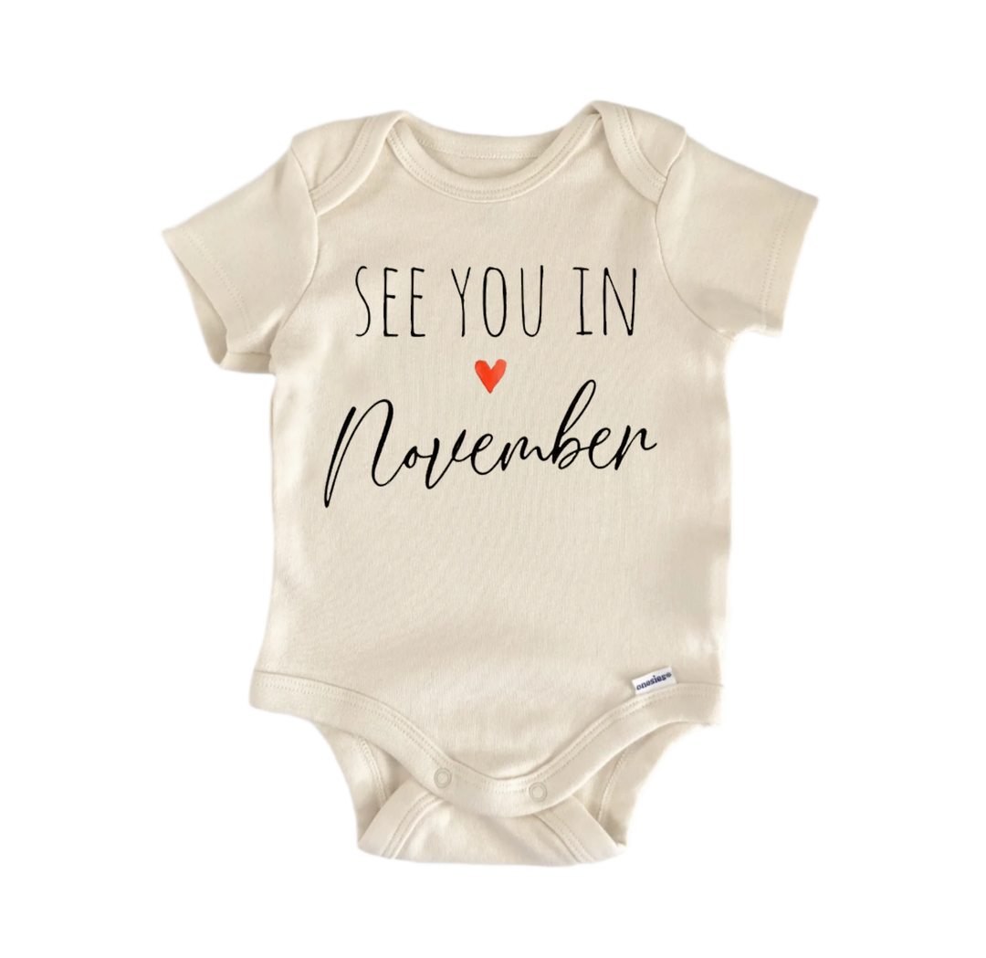 A beige baby onesie with the text "See you in November" printed on it.