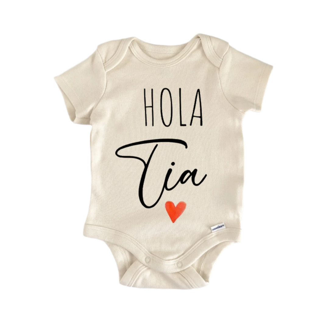 A beige baby onesie with the text "Hola Tia" printed on it, along with a small red heart symbol.
