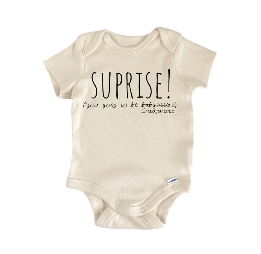 A beige baby onesie with the text "SUPRISE! [Your sons to be grandpa/ grandma] Grandparents" printed on it.
